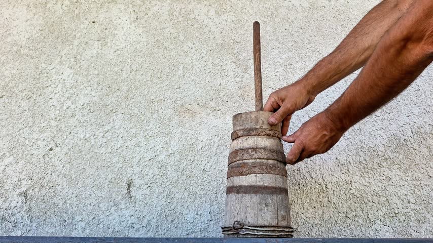 Traditional wooden butter churn with a perforated paddle being assembled by hand. Rustic dairy-making equipment showcasing a traditional method of homemade butter production tool