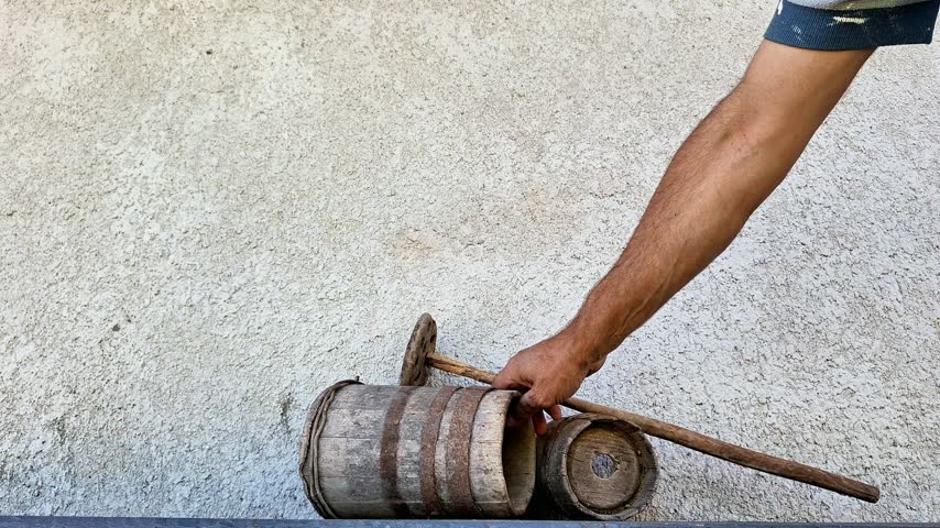 Wooden butter churn being used by hand to process cream into fresh homemade butter. Close-up of a rustic dairy-making tool and the manual churning process in a simple setting