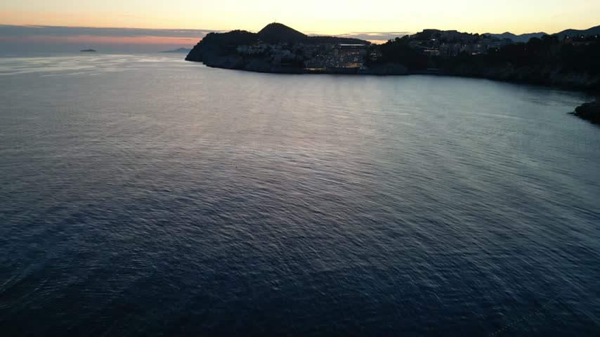Sunset Horizon Over Calm Adriatic Waters Along The Silhouetted Lapad Bay Coastline And Velika Petka Hill In Dubrovnik, Croatia. - aerial shot