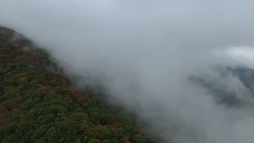 Stationary aerial view of clouds drifting across a mountainside covered in autumn trees along the Talimena National Scenic Byway in southeastern Oklahoma.