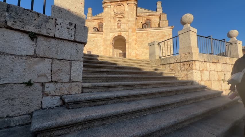 Revealing view of the historic Collegial Church of San Pedro Apostol while ascending the stone staircase on a sunny day in Lerma, Spain