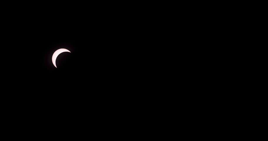 A partial solar eclipse moves across a dark black sky, highlighting the sun and moon alignment in timelapse.