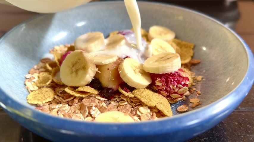 close up of cereal bowl with chopped fruits and milk being poured from above