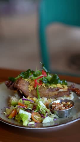 Close-up 4K footage of Indonesian crispy fried duck bebek goreng with sambal matah, fresh salad and rice on plate, traditional Balinese gourmet food on wooden table.