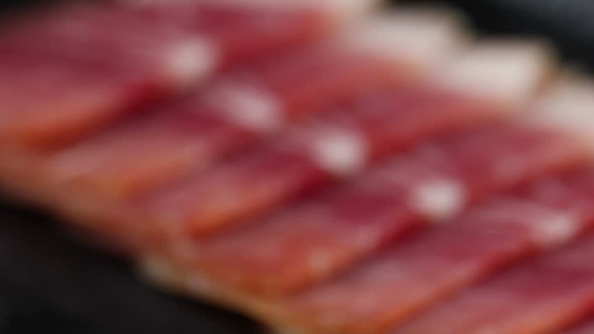 Close-up shot of thinly sliced cured ham arranged on a plate.