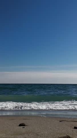 A grassy coastal landscape with a narrow path leading toward the sea under a clear blue sky. The shoreline and distant horizon are visible on a sunny day.