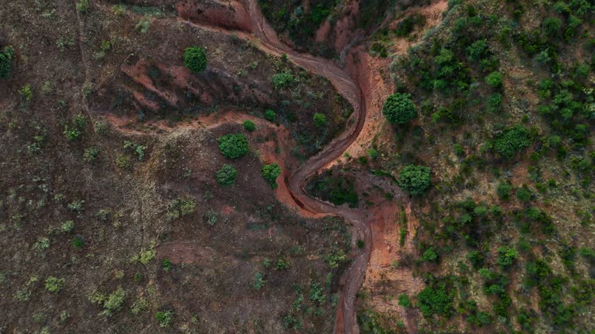 Aerial view of a landscape of eroded reddish hills, with steep ridges and scattered patches of green shrubbery