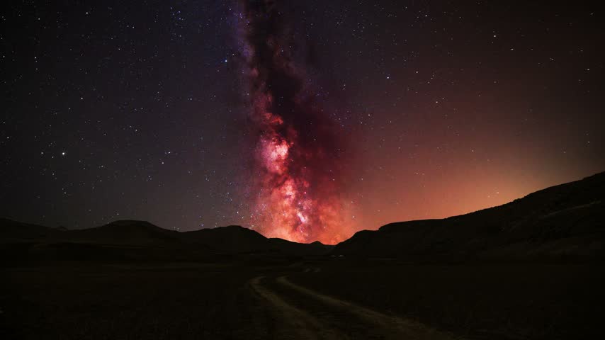 The bright, colorful Milky Way galaxy in the night sky above a hills and mountains.