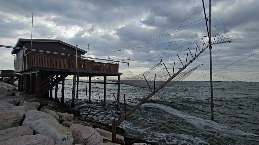 Wooden Fishing Hut on Stilts Over Rocky Coast With Nets and Cloudy Sea Sky