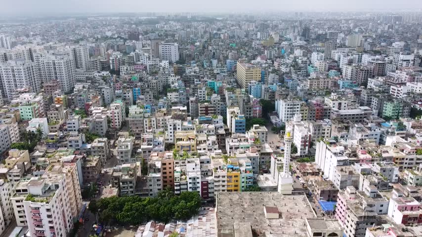 Aerial drone footage showing the dense urban landscape of Dhaka, Bangladesh, with residential buildings, rooftops, city architecture and a mosque in the metropolitan area.