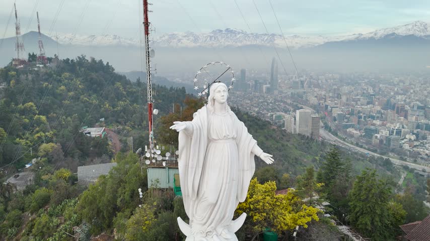 Virgin Mary statue on San Cristobal Hill during bright sunny day, revealing Santiago city skyline, Chile.