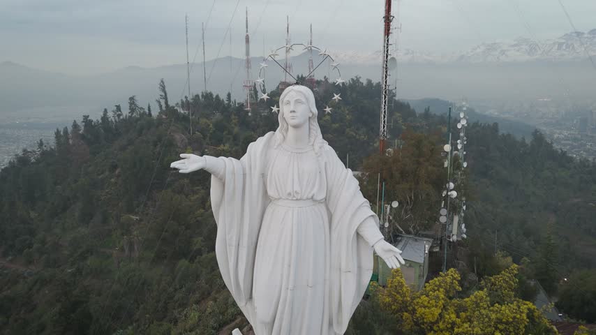 Virgin Mary statue on San Cristobal Hill during bright sunny day, revealing Santiago city skyline, Chile.