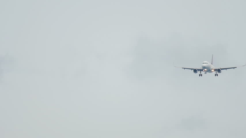 Twin-engine passenger airplane on final approach descending toward camera in overcast gray sky, landing gear down, front view telephoto shot.