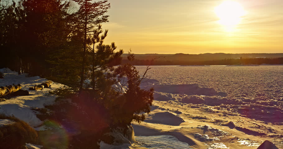 Rightward pan moves across a warm winter sunset over frozen Lake Superior with snow-covered shoreline and silhouetted trees near Marquette.
