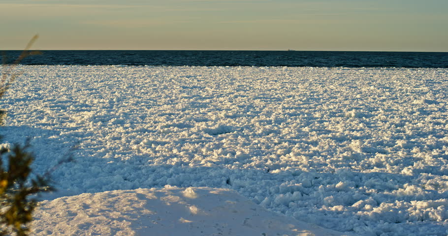 Slow rightward pan crosses a broad field of broken and packed shore ice with a narrow strip of open Lake Superior water beyond.