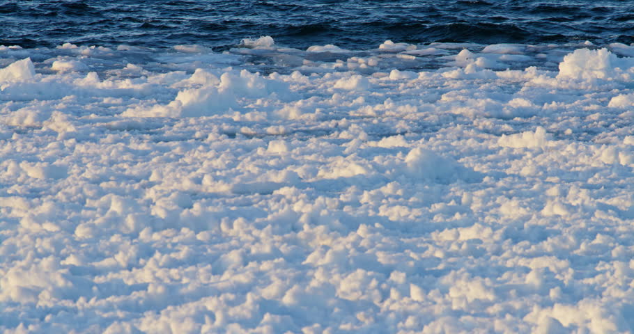 Static winter view shows dark open Lake Superior water moving behind a dense field of broken white shore ice along the Marquette shoreline.