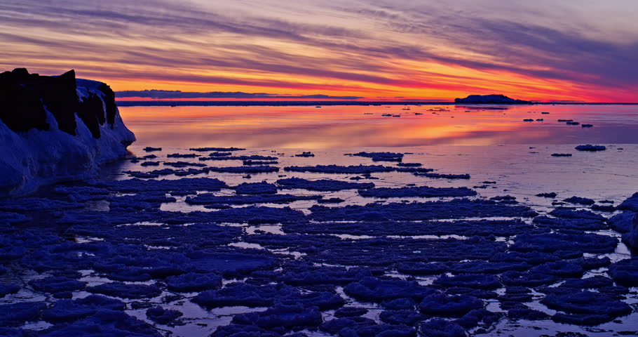 Vivid winter sunset spreads pink, orange and purple light over Lake Superior pancake ice and dark basalt shoreline at Presque Isle Park in Marquette.