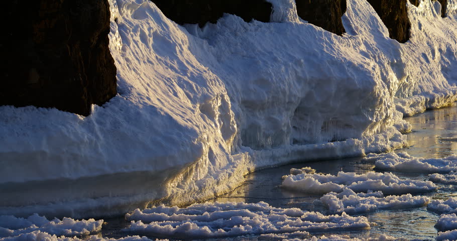 Slow rightward pan follows thick snow and ice layered across dark basalt shoreline beside floating Lake Superior ice at Presque Isle Park.