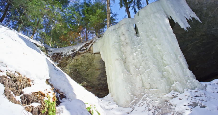 Descending camera move follows the tall ice curtain from the sandstone ledge toward its frozen base at the Eben Ice Caves in Michigan
