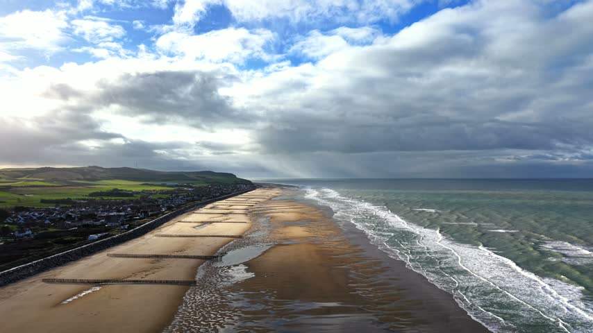 Aerial view of a beach with wooden groynes and tidal channels as the sun breaks through the clouds at Sangatte near Calais, northern France