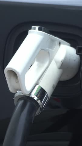 Black Electric Car Charging at Station. Connector Attached to Vehicle in Close Up.