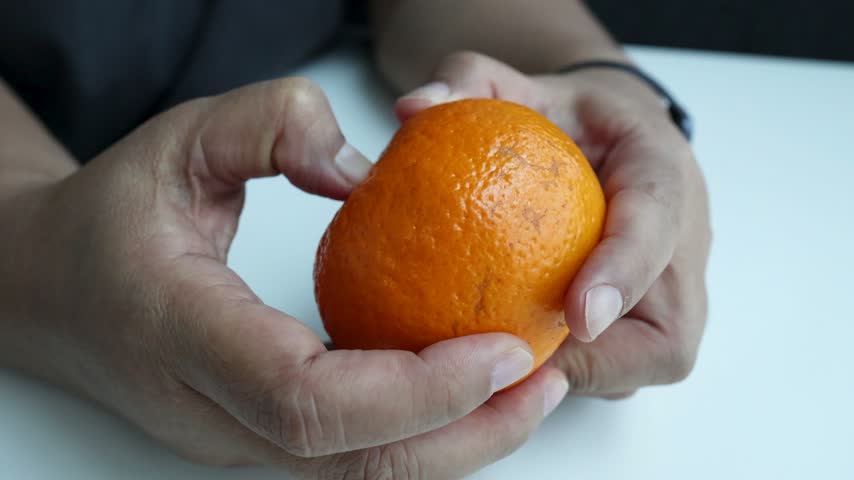 Close-up of person hands carefully peeling fresh ripe mandarin orange on white table surface.