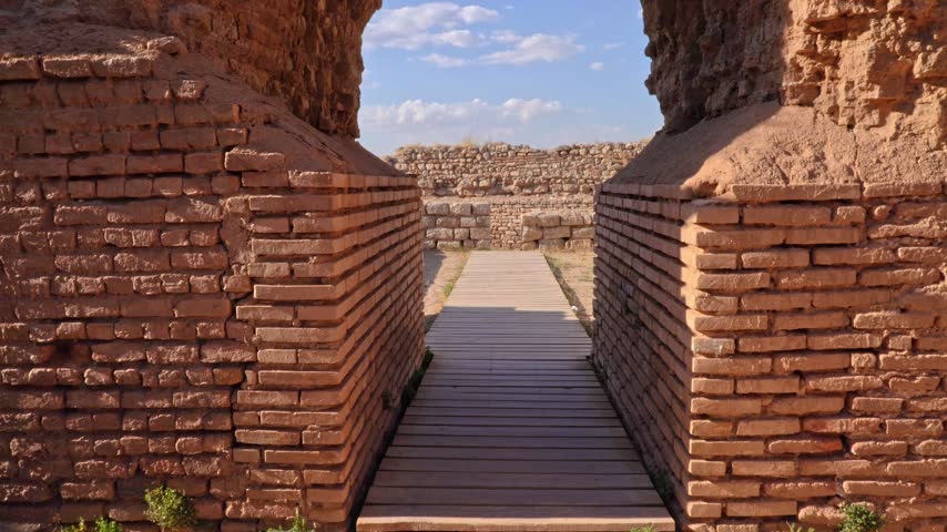 Tilting up over the ancient brick arch frames a wooden walkway through the ruins of Takht-e Soleyman, Iran