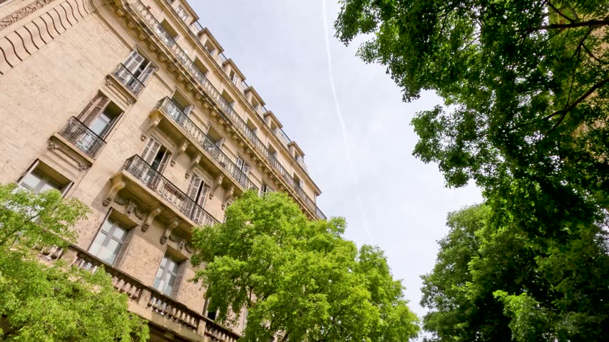 Low-angle view of classic Haussmann apartment facade framed by lush trees in Marseille, France.