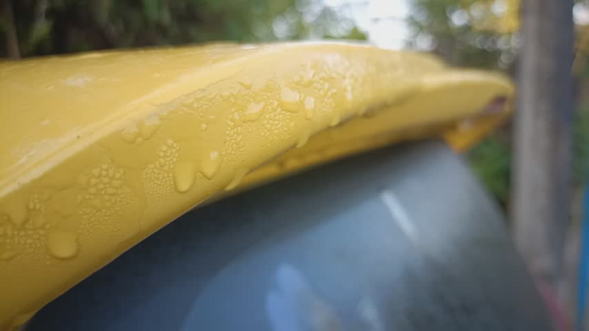 Close up view of morning dew water droplets on a yellow car spoiler surface