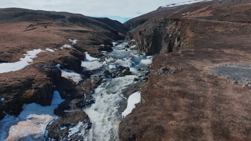 Mountain river cutting through snowy rocky canyon under bright sun