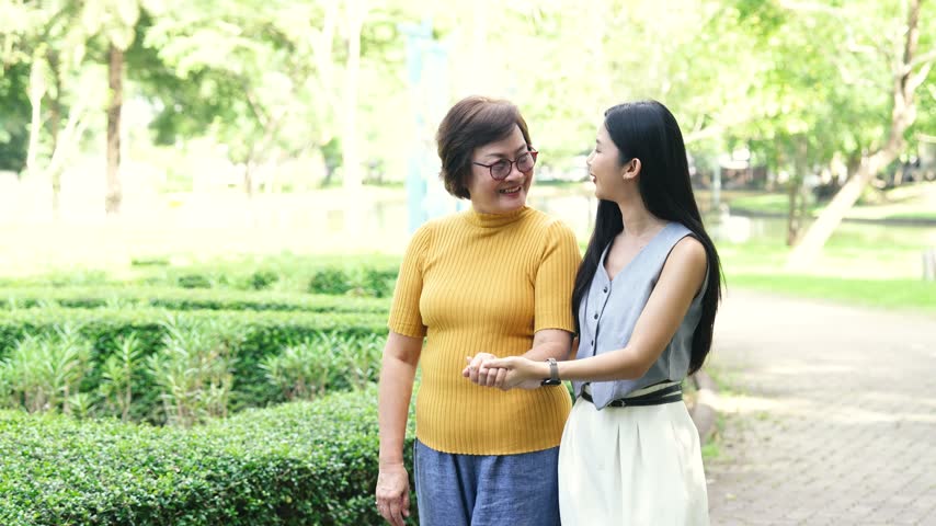 Mature woman using a walker with support from a younger woman in a park, representing elderly care, mobility assistance, rehabilitation, and family support.