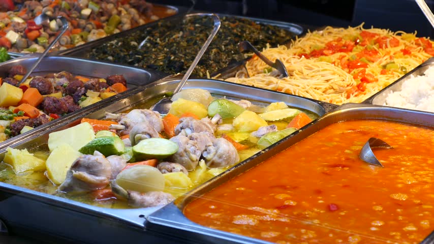 Close up camera panning motion capturing assortment of colorful healthy food options inside industrial metal containers placed along buffet service counter for catering events.
