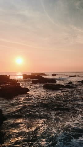 Sunset over rocky ocean waves washing ashore