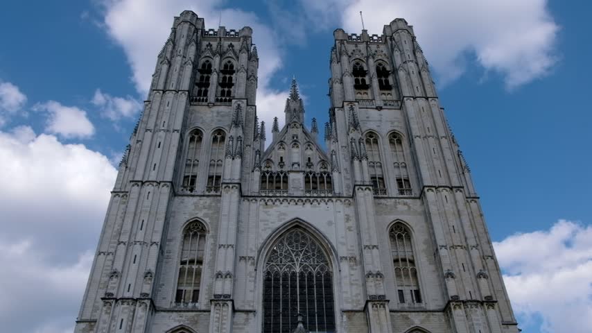 Dramatic low angle shot capturing Gothic architecture of Saint Michael and Saint Gudula Cathedral in Brussels with flowing clouds.