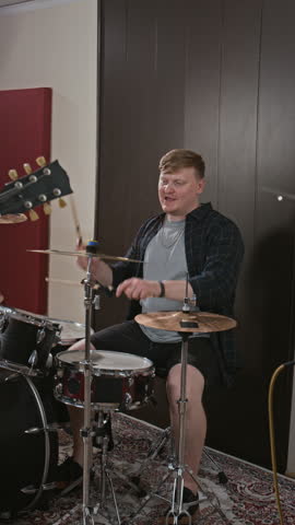 Vertical shot of Caucasian young adult men playing drums and electric guitar during rock band rehearsal. Footage fits music academy ads and entertainment campaigns