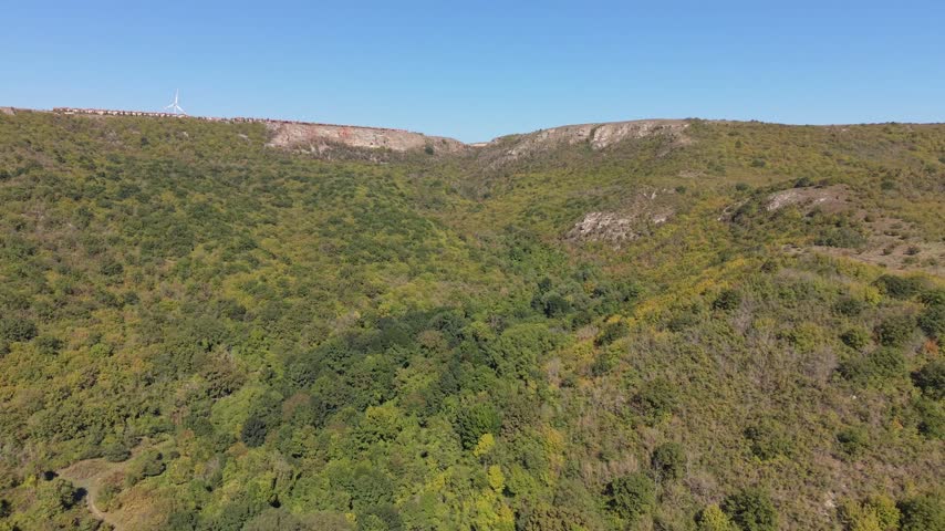 High aerial perspective reveals rocky terrain, green hills, shrubs, and peaceful countryside.
