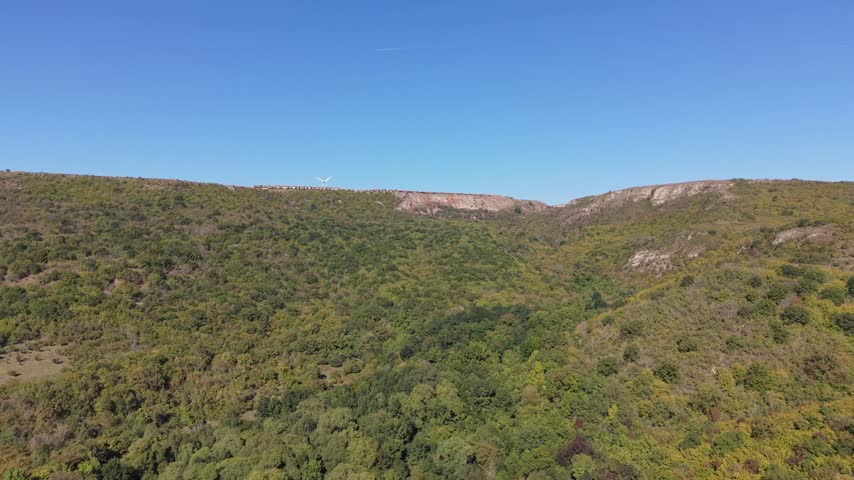 Natural aerial scenery featuring rocky hills, green shrubs, and bright blue skies.