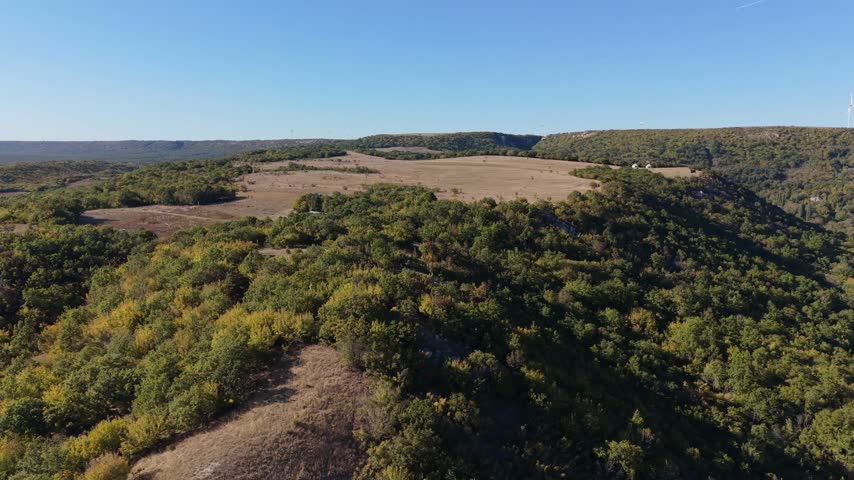 Panoramic aerial footage captures peaceful forested hills stretching beneath a clear blue sky.