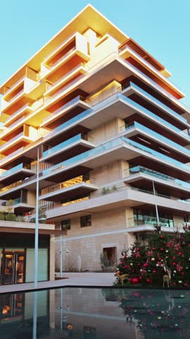 Stunning low angle shot of contemporary residential building facade during sunset featuring Christmas tree and reflective pool.