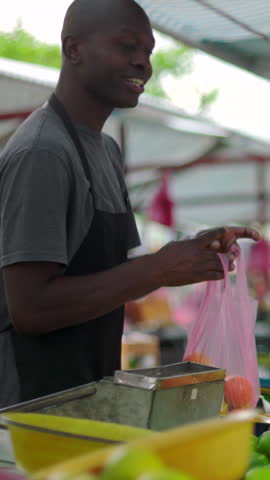 Local African American produce seller passing bagged ripe oranges across the counter to a shopper during everyday neighborhood food commerce