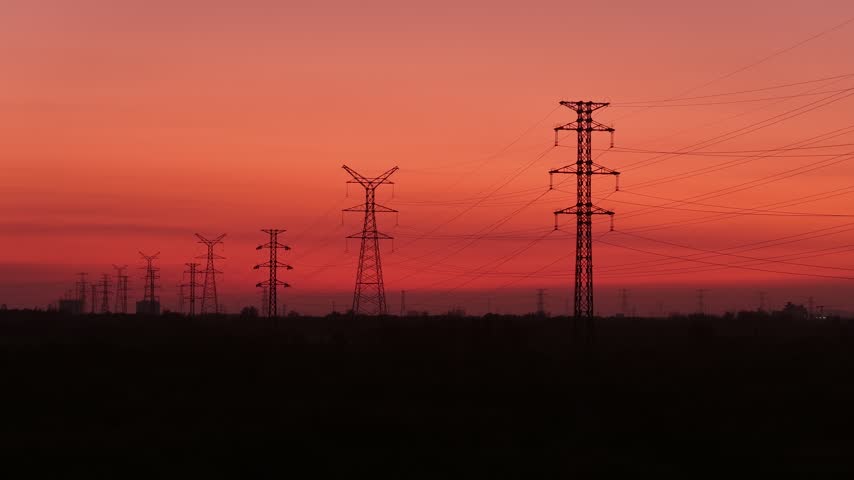 silhouette of high voltage transmission towers against a red sunset sky