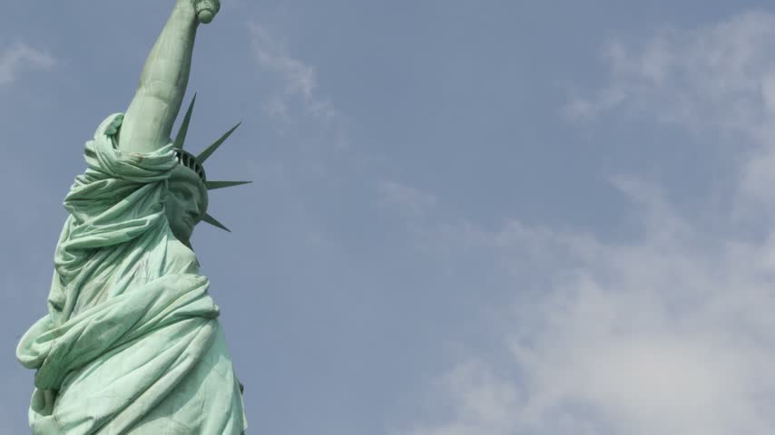 Statue of Liberty on Liberty Island, New York, United States. Blue cooper monument, symbol of democracy and patriotism near Manhattan, NYC USA. Clouds on sky. American independence. Torch and crown.