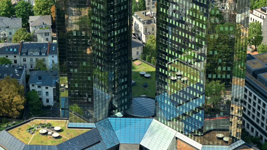 High angle shot of contemporary architecture with reflective glass windows showing city streets and urban park vegetation.