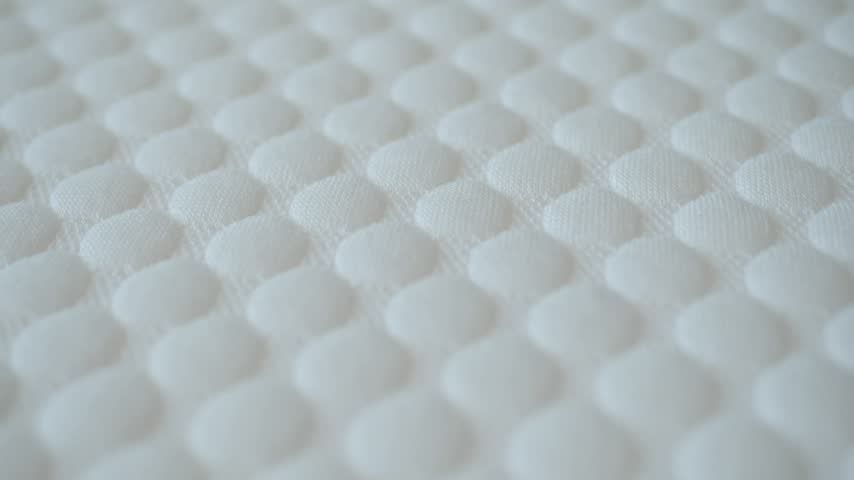 Close up shot showing human hand pressing into comfortable white quilted mattress cover demonstrating soft material quality and memory foam technology ideal for bedding advertising.
