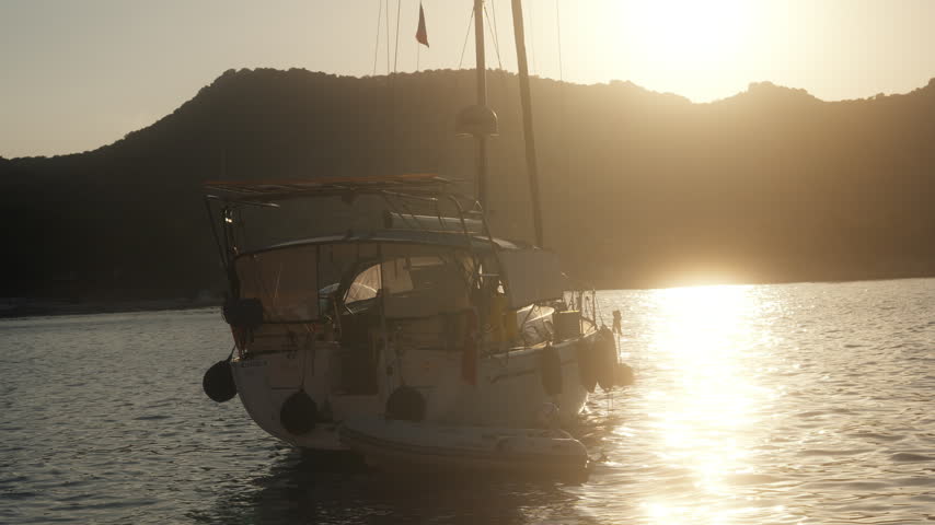 Sunset view of a boat anchored near the shore with mountains in the background during the evening