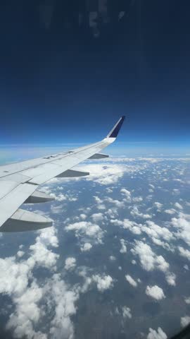 Aerial view from airplane window showcasing wing in clear blue sky over clouds.