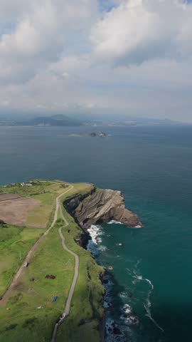 Volcanic Cliffs And Coastal Walking Trail Towards Songaksan Peak Viewpoint Overlooking Hwanguchi Beach In Seogwipo, Jeju Island, South Korea. - aerial vertical shot
