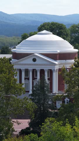 The UVA Rotunda fills a vertical frame in Charlottesville, Virginia, with its white dome, columned portico and red brick walls above the trees. Aerial view