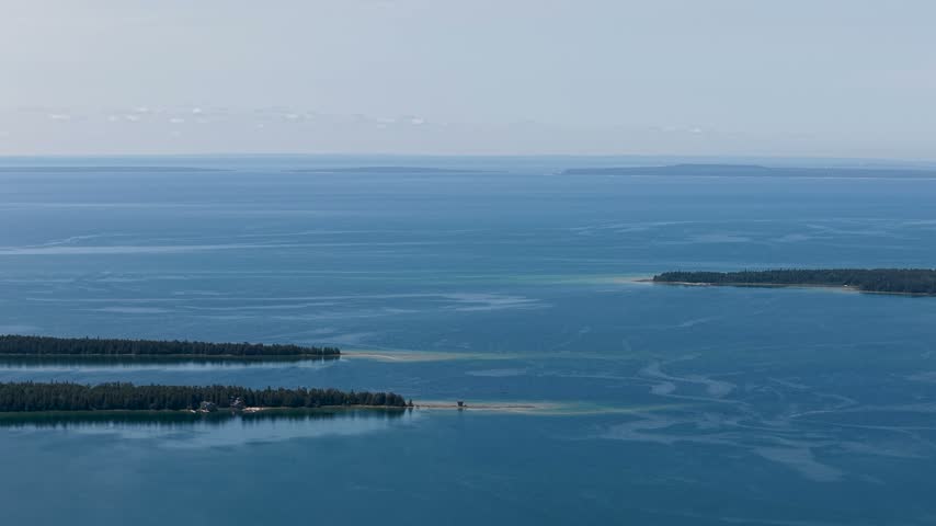 Wide aerial panorama of calm blue Lake Huron stretching beyond low wooded islands near Hessel in the Upper Peninsula of Michigan.