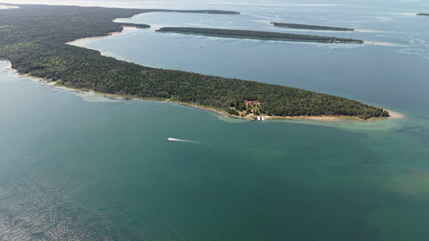 A small motorboat leaves a white wake beside a wooded point and long low islands on Lake Huron near Hessel Michigan.